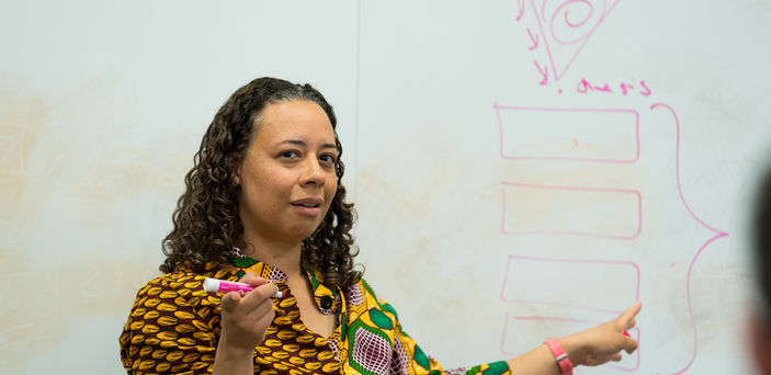 Dr. Allyson Ferrante teaches in front of a white board that she is pointing to while holding a marker in her other hand