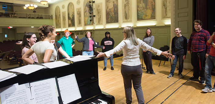 BSU professor forms a circle on stage with students next to her piano