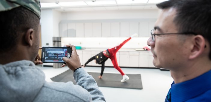 BSU biomechanics class with 1 student doing a cartwheel while another video records it and the professor looks on