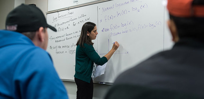 BSU Math professor Rachel Stahl writes on a white board under the words "Natural Logarithm function" while students look on