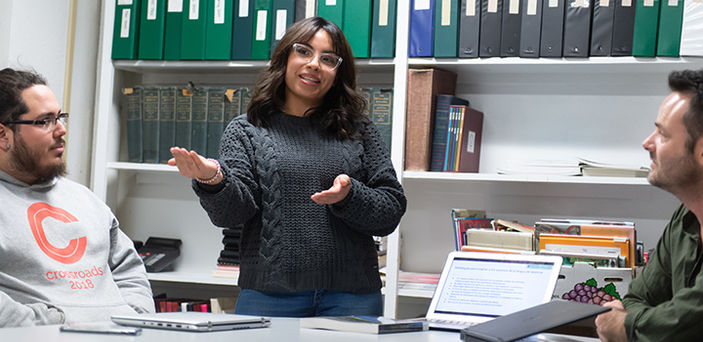 A student giving a presentation in Spanish while Professor Ryan LaBrozzi and another student look on