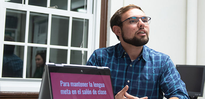 A student gives a presentation in Spanish next to his open laptop that shows the title of the presentation in Spanish