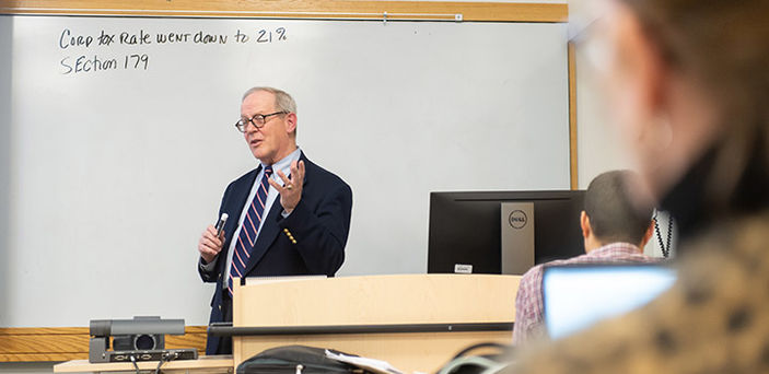 Professor Mark Crowley teaching in front of a white board with notes on the corporate tax rate