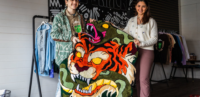 Megan and Matt hold up a rug with a tiger 