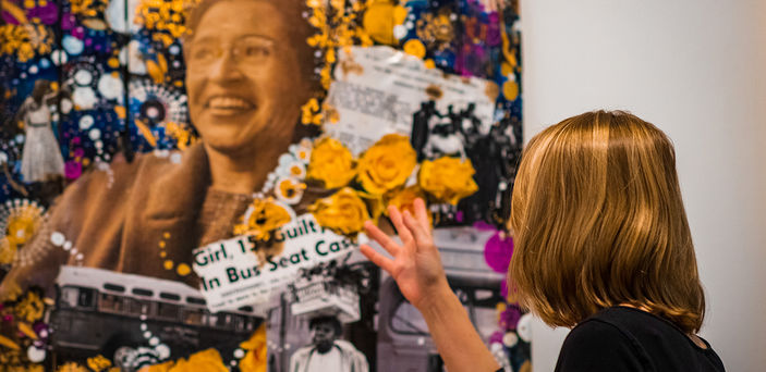 Elizabeth Ezekiel gestures at art featuring newspaper clips and a portrait.