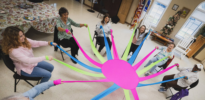 Students and elders move a large, colorful fabric together.