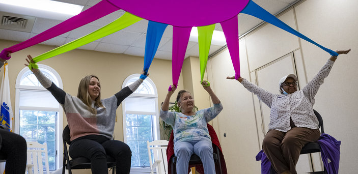 Students and elders move a large, colorful fabric together.