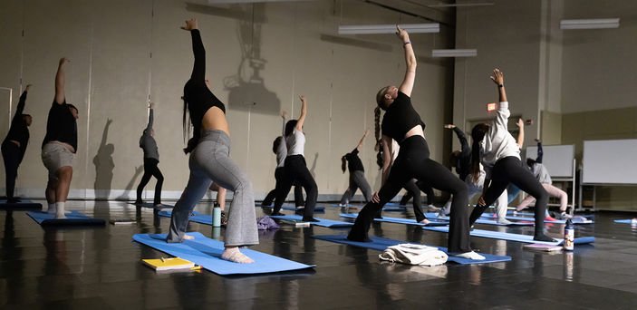 Students lean to the side and stretch their arms during a yoga exercise.