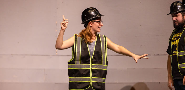 A student points into the air while wearing construction clothes