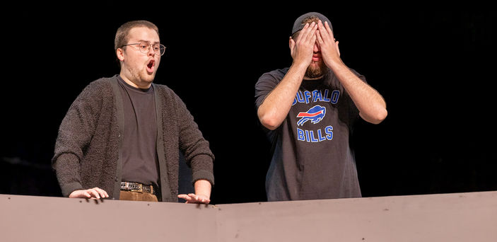 A student holds hands over their face while another student sings