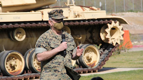 Anthony LaCourse speaks to a crowd standing in front of a tank.