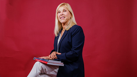 Dr. Lisa Battaglino sits on a stool holding books in front of a red backdrop.