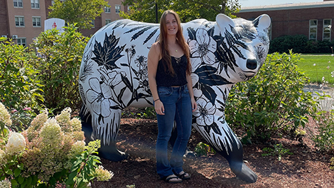 Sam Cushman stands in front of the bear statue she painted with images of native plants.