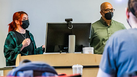 Carrie Provost stands next to a computer giving a presentation to students.