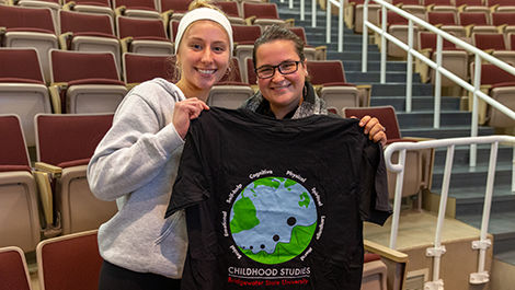 Two students hold a childhood studies t-shirt showing a globe.