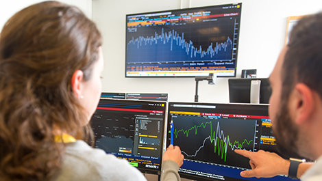 People collaborate at computers showing financial markets.