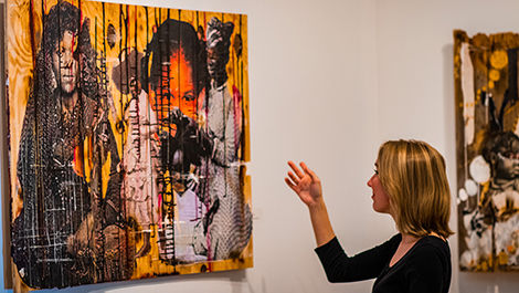 Elizabeth Ezekiel points at a fence panel covered in a collage in the art gallery.