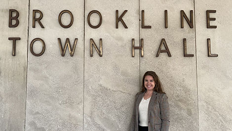 Devon Fields stands in front of a sign saying "Brookline Town Hall"