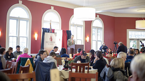Students and parents sit at round tables in Flynn Dining Commons listening to a speaker.