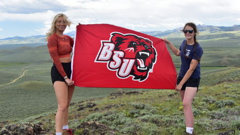 Olivia and Julia hold a red flag with the BSU bear logo in the Montana mountains.