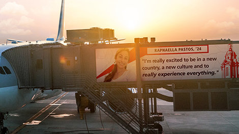 Graphics of a plane at a gate with a quote from Raphaella Pastos on the jetway saying "I’m really excited to be in a new country and a new culture and to just really experience everything"