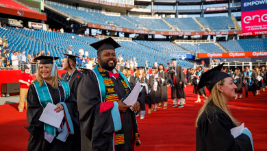 Graduates wearing caps and gowns walk towards the stage