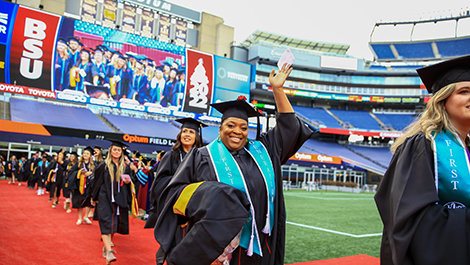 A graduate waves to the crowd while walking to her seat.