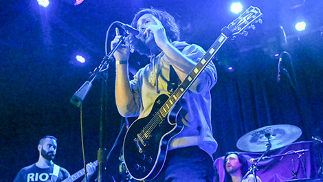 Matt Guilherme plays guitar and sings on a stage.
