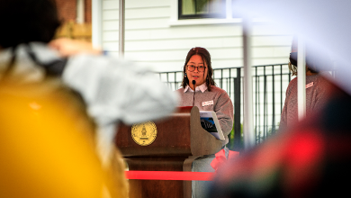 Joanne Tanaka stands behind podium and delivers a speech