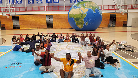 The Mandela fellows hold hands while sitting on a floor map of Africa.