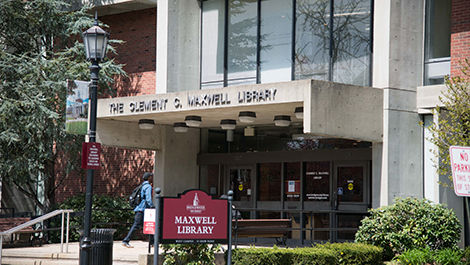 The exterior main entrance to Maxwell Library with a red sign displaying the building's name.