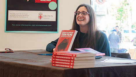 Michele Meek sits at a table with copies of her book on display
