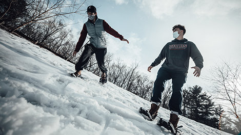 Two students snowshoe down a hill.