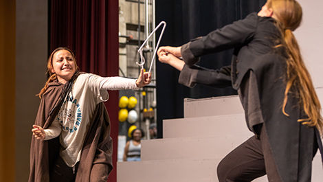 Two students rehearse a scene using a broken hanger as a prop.