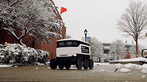 A food delivery robot travels on a campus sidewalk.
