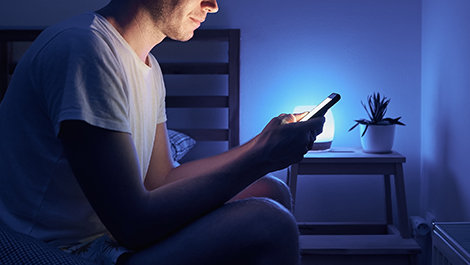 A person texts on a phone while sitting on a bed.