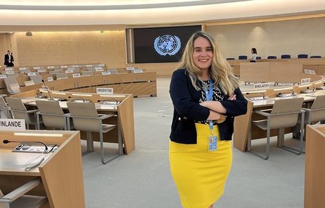Tiana wears a yellow skirt standing in the assembly room in the United Nations in Geneva