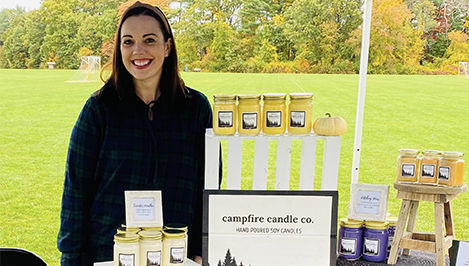 Ashley Twigg stands behind a display of her candles at an outdoor event.
