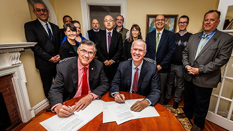UMass and BSU administrators stand around a table to sign a document.