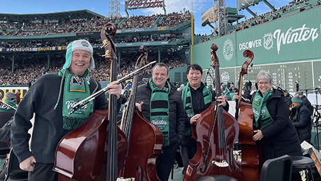 Bass players stand in front of the Green Monster and Fenway Park stands.