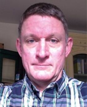 headshot photo of professor Andrew Armstrong with short greyish brown hair wearing a blue, white and green plaid button down shirt with collar