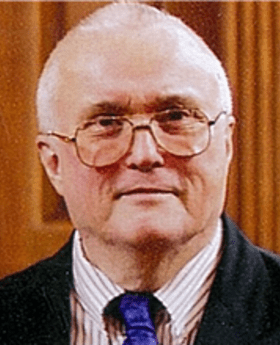 headshot photo of Dr. Charles Cox wearing dark blazer, striped button down shirt and blue tie