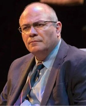 Dr. Francisco Alatorre balding with short gray hair wearing brown rim glasses a light blue button down shirt, navy blue tie and blazer