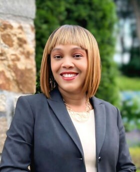 Sandy Beauvoir smiling with medium length straight blondish brown hair and wearing a gray blazer over a cream colored top