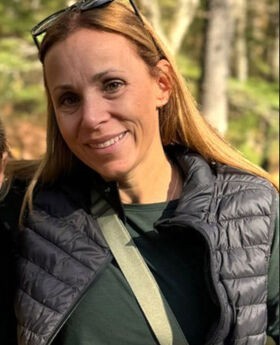 Kristen Buchanan smiling with long light brown hair and wearing a black vest over a long sleeve green top