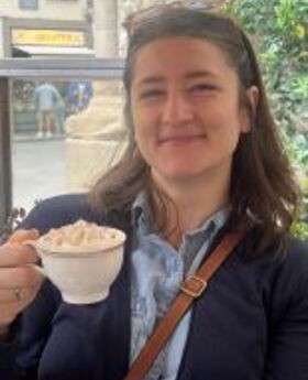 Juliette Coatsworth smiling with medium lengthbrown hair and wearing a navy blue blazer over a button down light blue shirt.