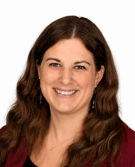 Dr. Michelle Commeret smiling with long wavy brown hair and wearing a  maroon blazer over a black top