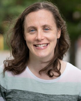 Dr. Robin Dawson smiling with long brown hair and wearing a long sleeve top with wide horizontal bands of white, light blue and gray