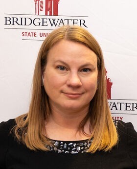 Dr. Emily Field smiling with straight medium length light brown hair wearing a black top with crystals around the neckline