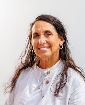 Tammy Greene smiling with long brown hair and wearing a white button up jacket over a white top